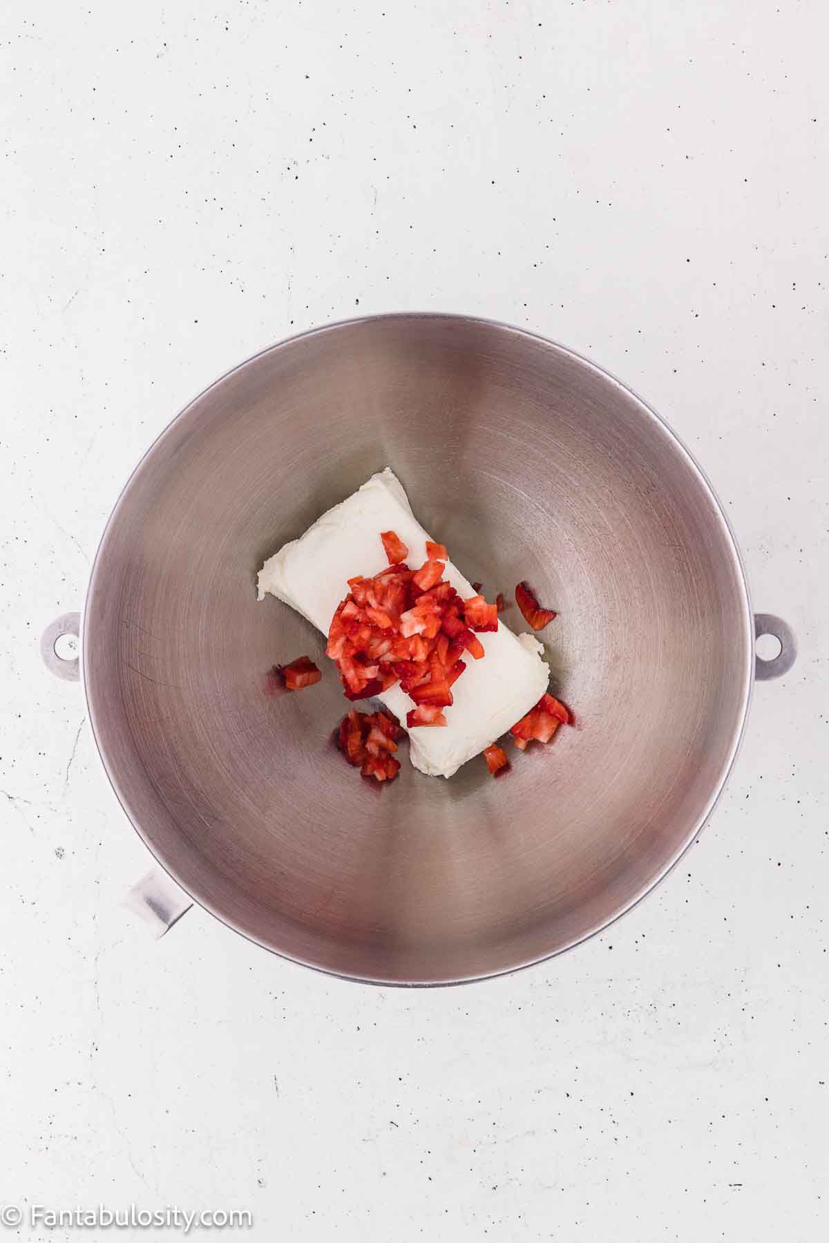 Cream cheese with chopped strawberries in a mixing bowl.