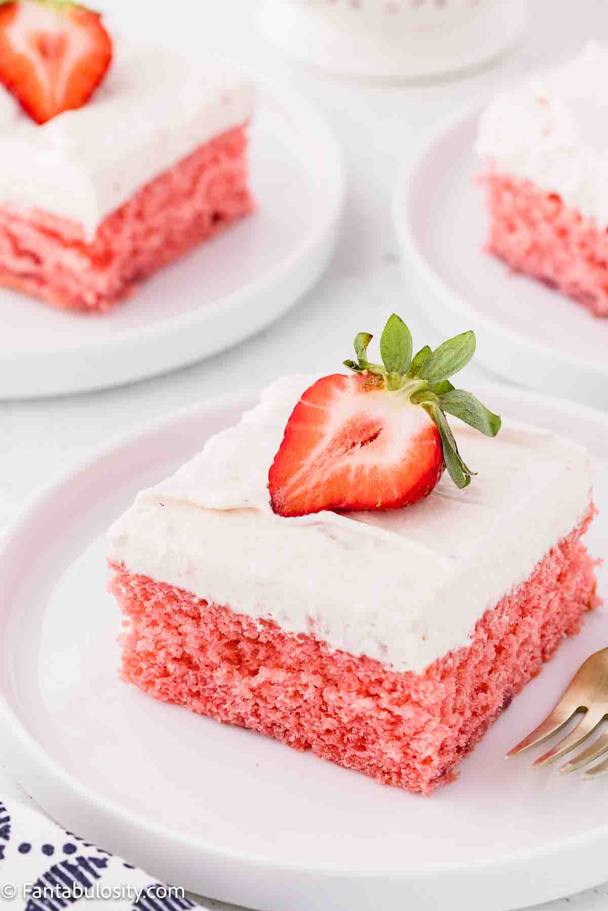 A slice of strawberry jello cake topped with a sliced strawberry, sitting on a plate.