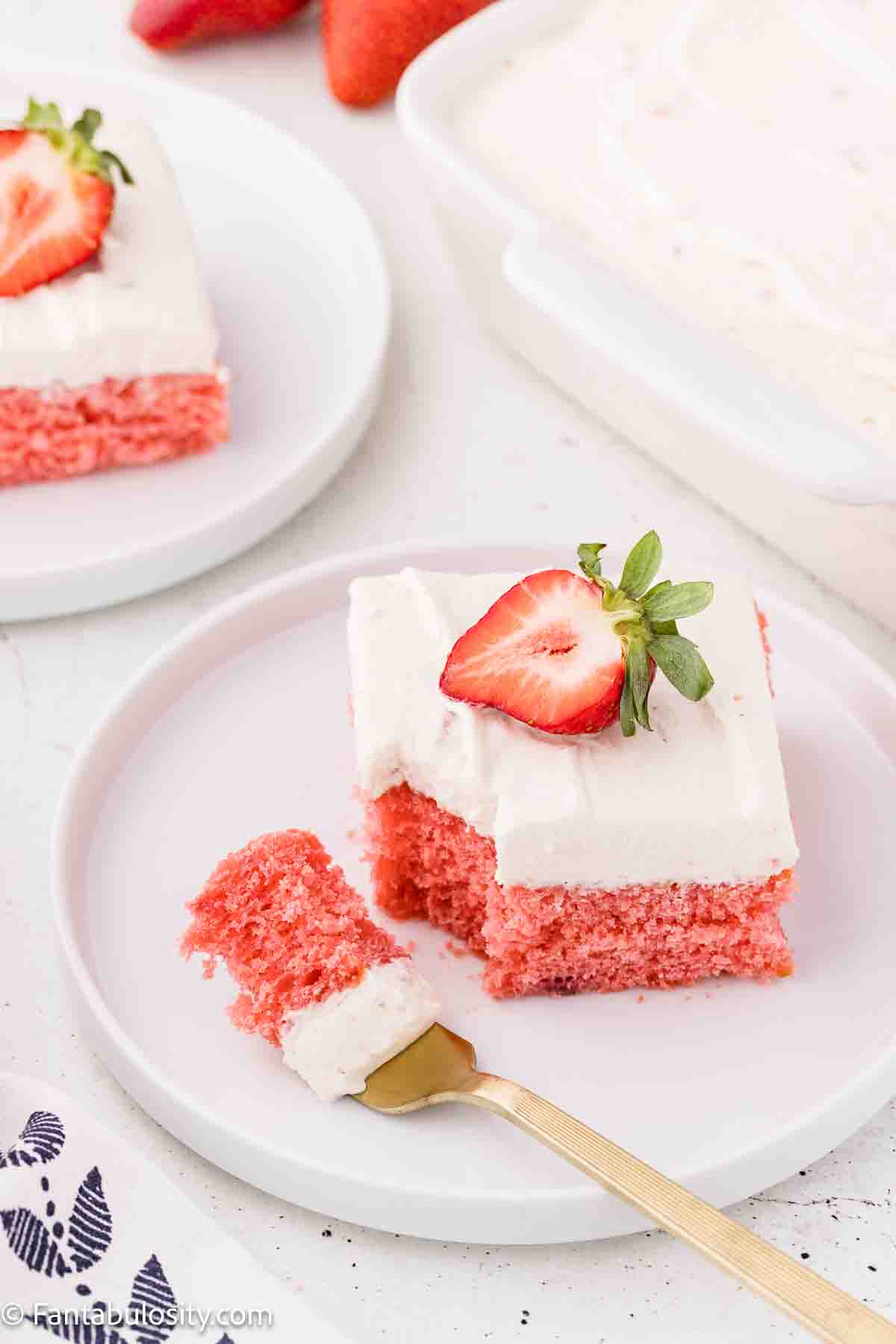 A slice of strawberry cake with strawberry cream cheese frosting sitting on plate, next to fork.