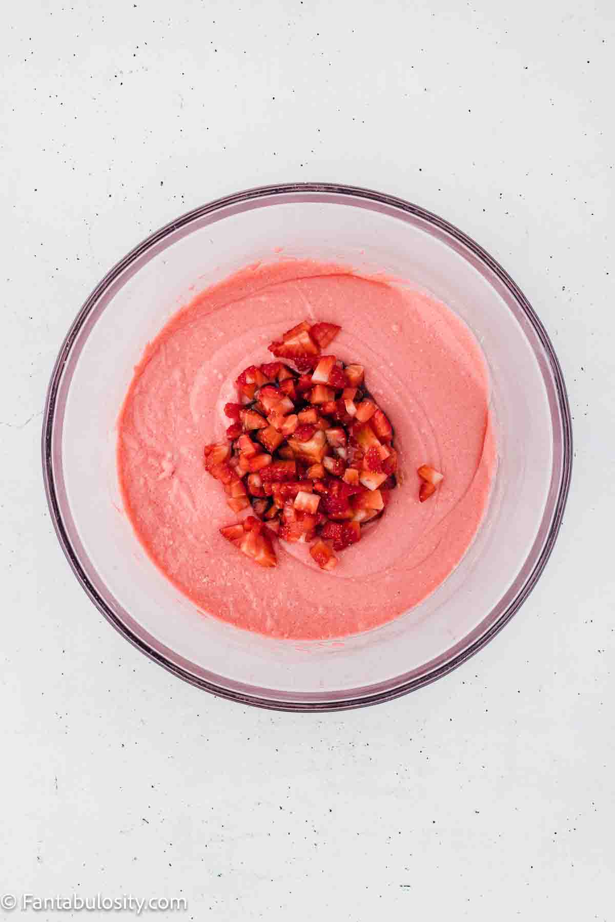 Chopped strawberries added to strawberry cake mixture batter, sitting in mixing bowl.