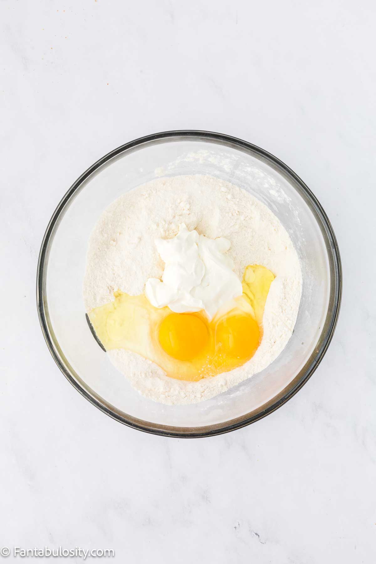 Eggs and sour cream added to Texas Sheet cake dry ingredients in mixing bowl.