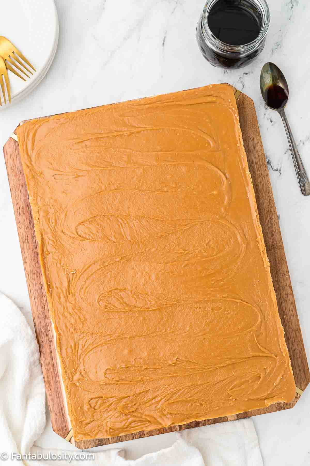 Burnt sugar cake, frosted, sitting on wooden cutting board.