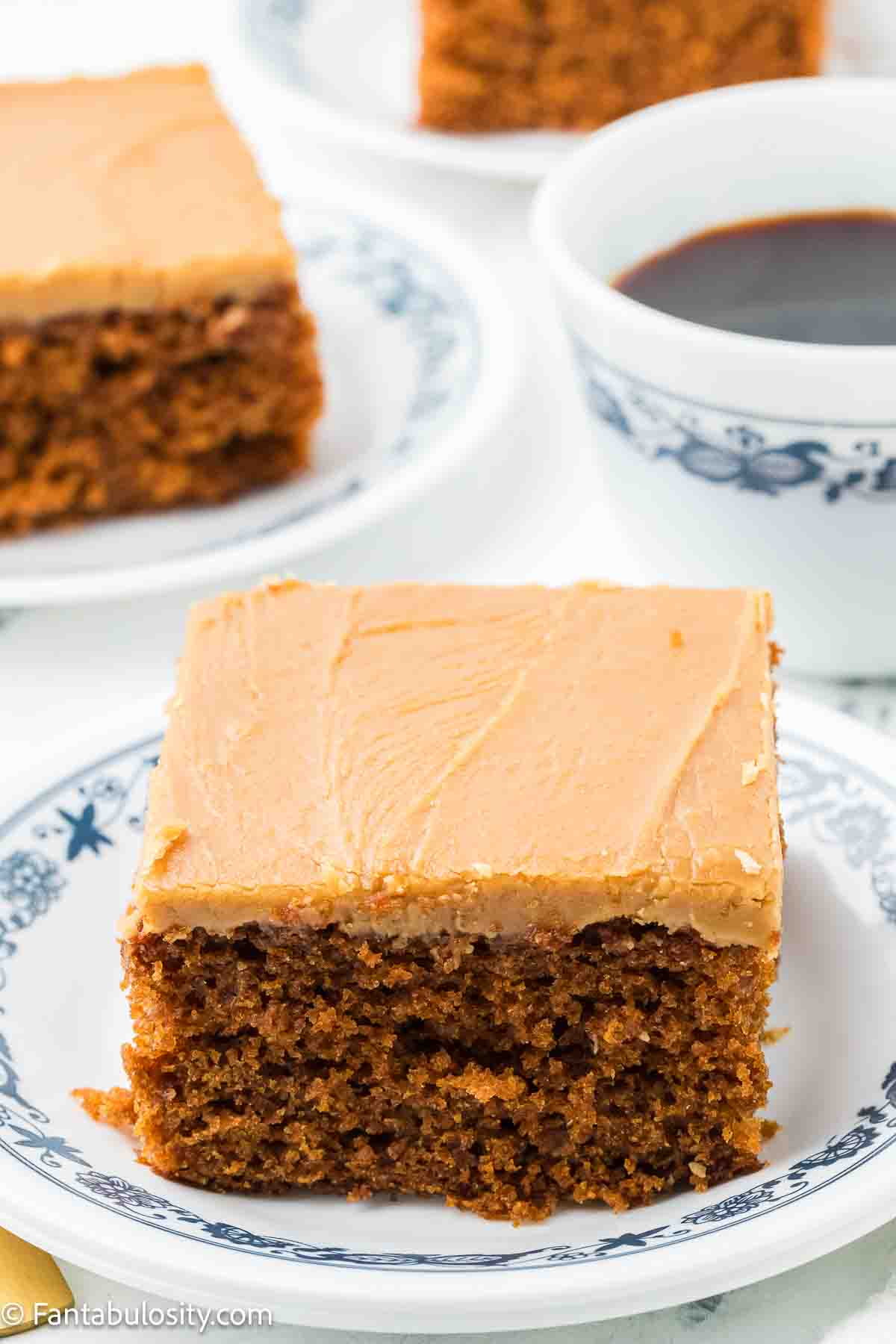 A slice of burnt sugar cake on a round, vintage plate, sitting next to a cup of coffee.