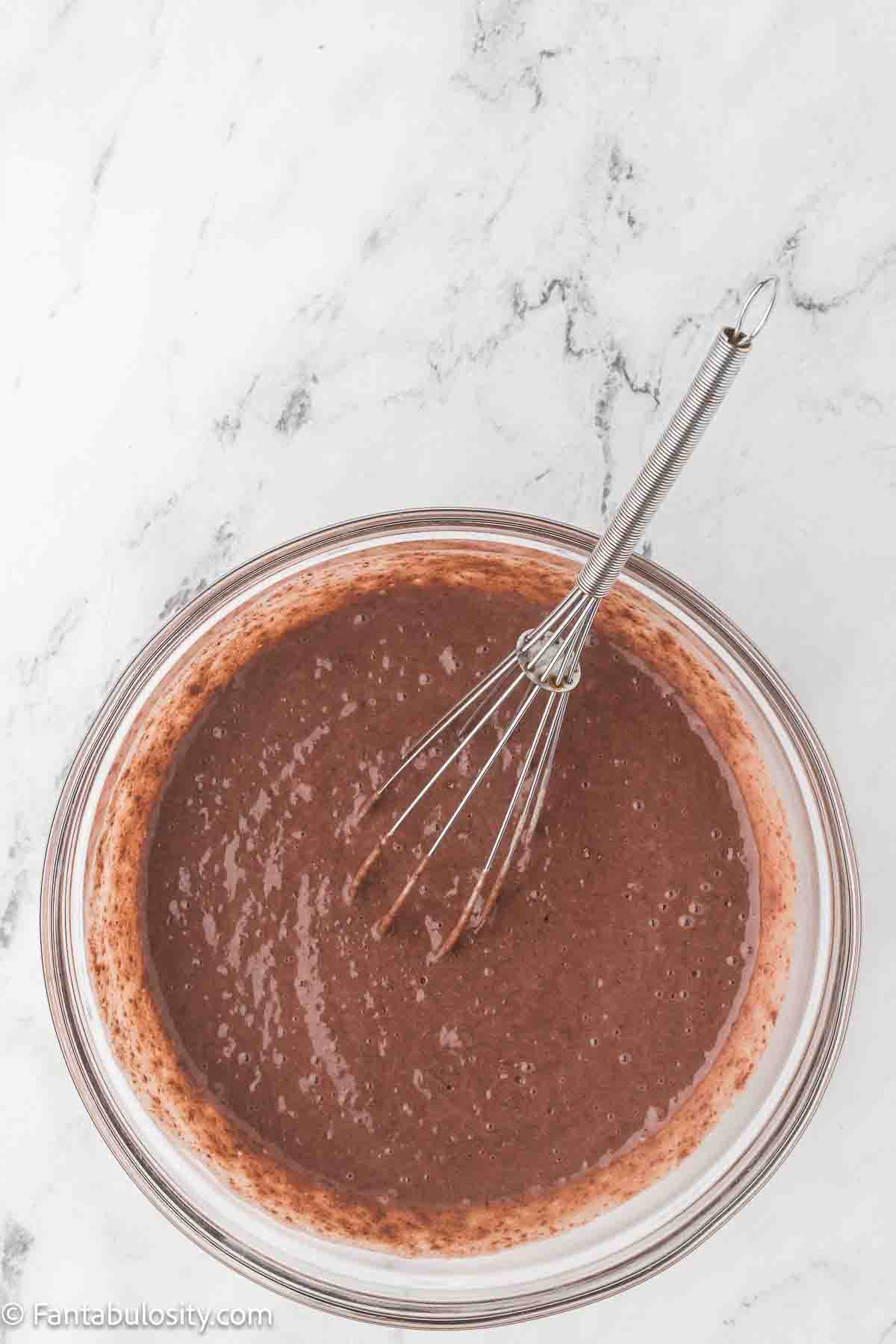 Chocolate pudding mix and milk in glass mixing bowl.