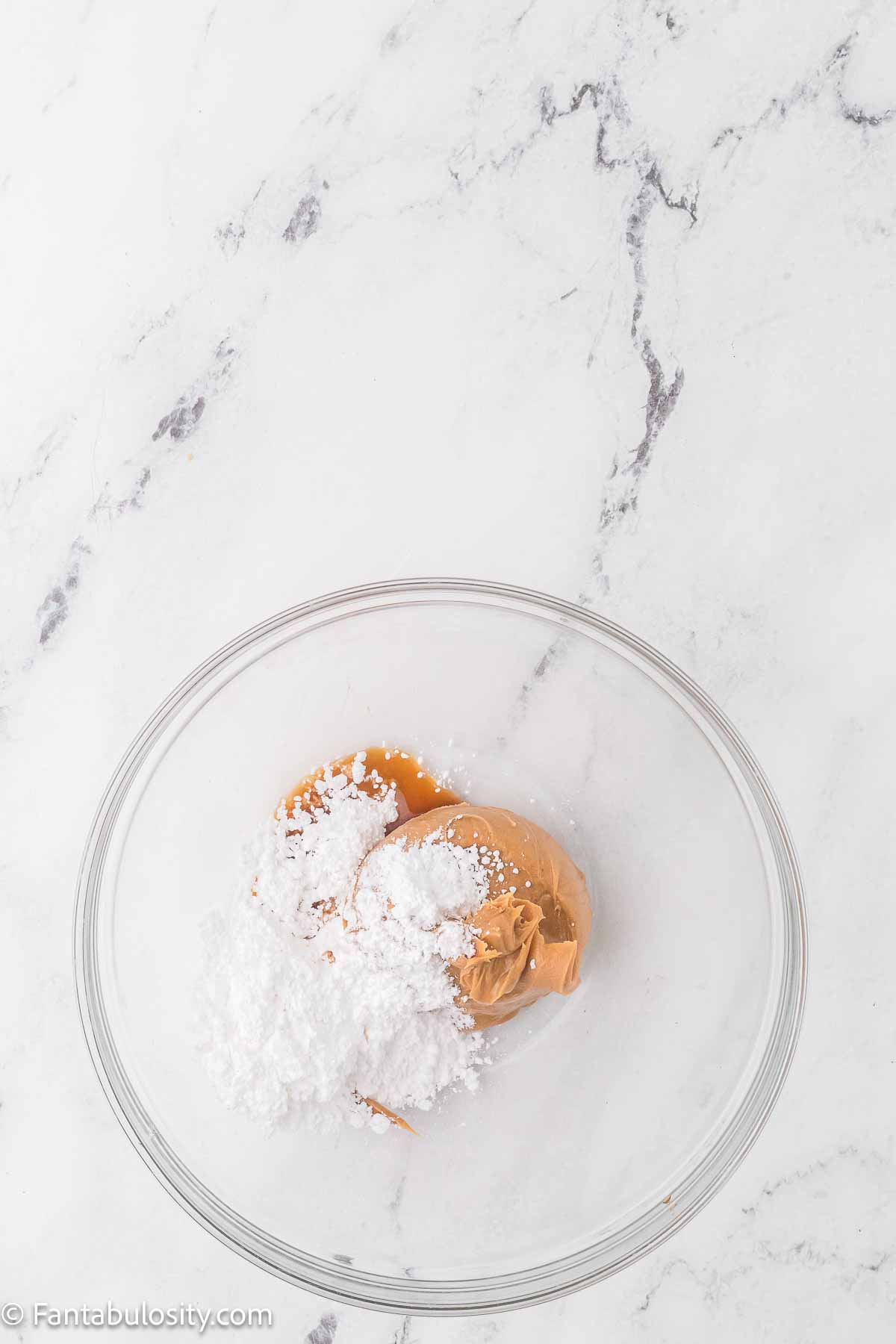 Peanut butter and powdered sugar in clear mixing bowl.