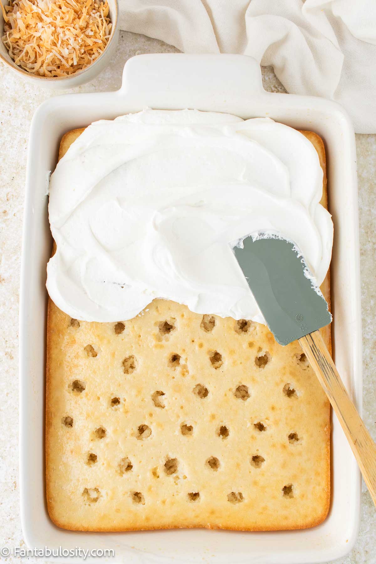 Frosting spread on top of coconut poke cake.