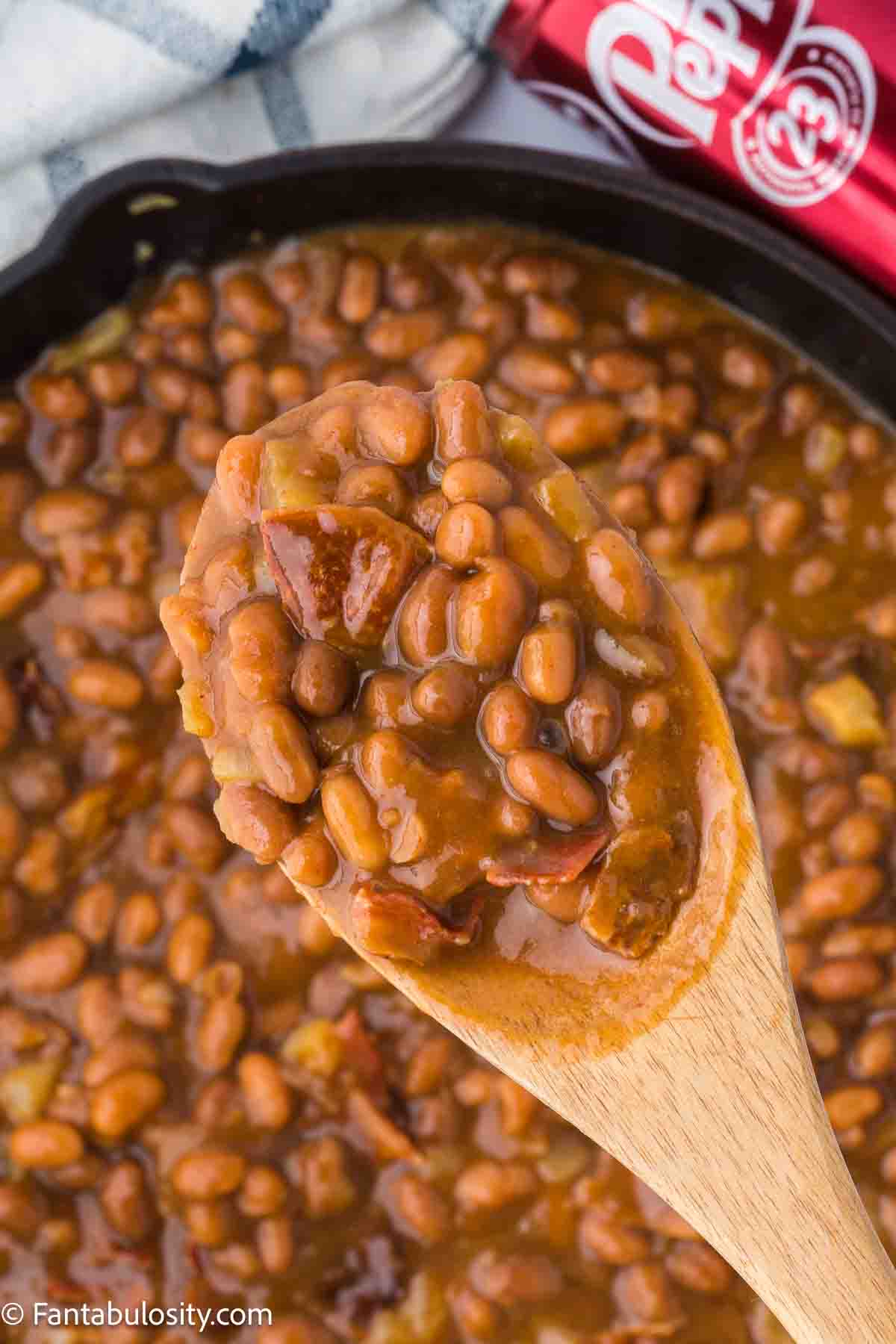 Wooden serving spoon holding a serving of Dr. Pepper Baked Beans.