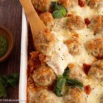 A wooden spoon dishing out a serving of meatball casserole in a 9x13 baking dish.