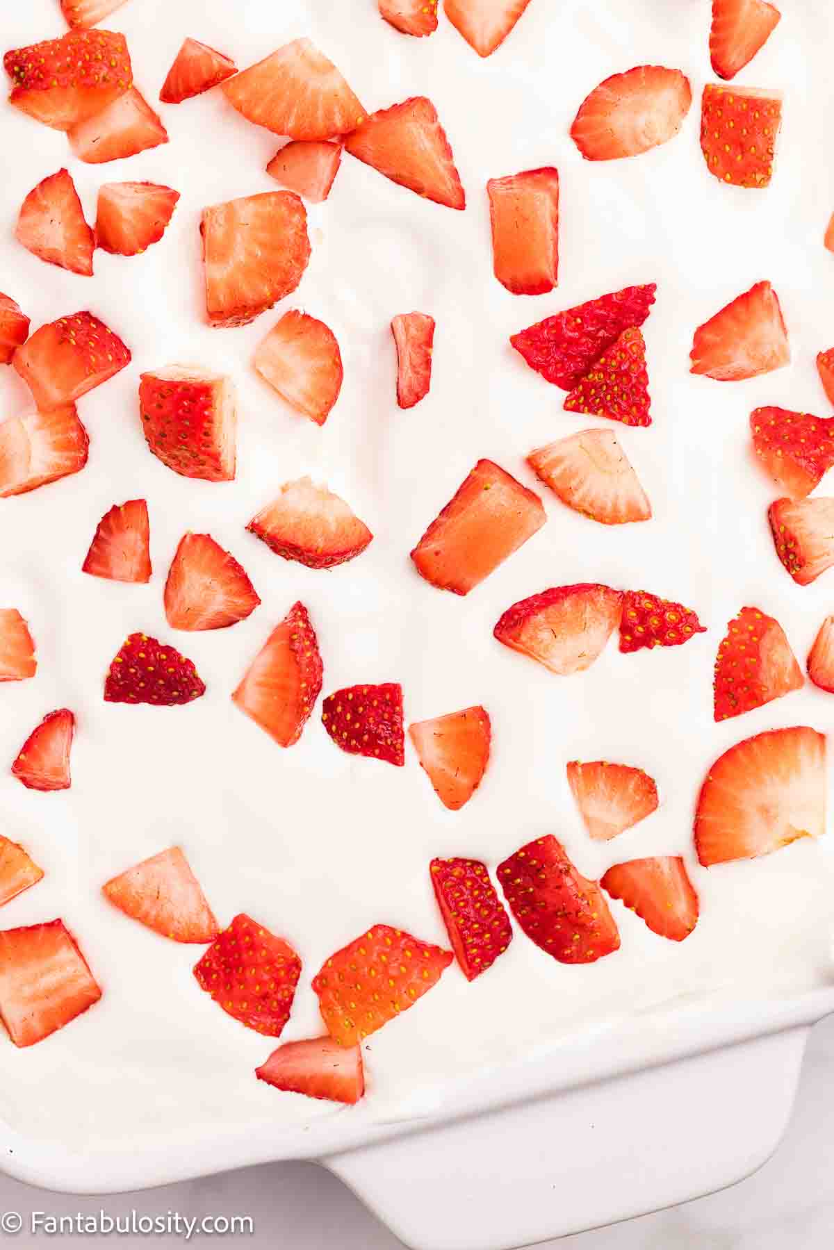 Diced strawberries sprinkled on top of Cool Whip topping on cake.