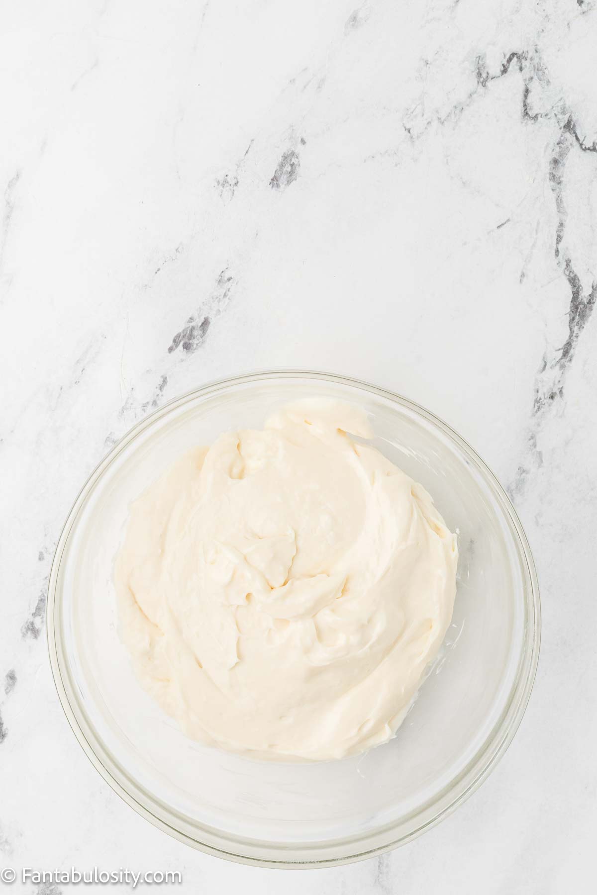Cream cheese, sugar and vanilla mixed in glass mixing bowl.