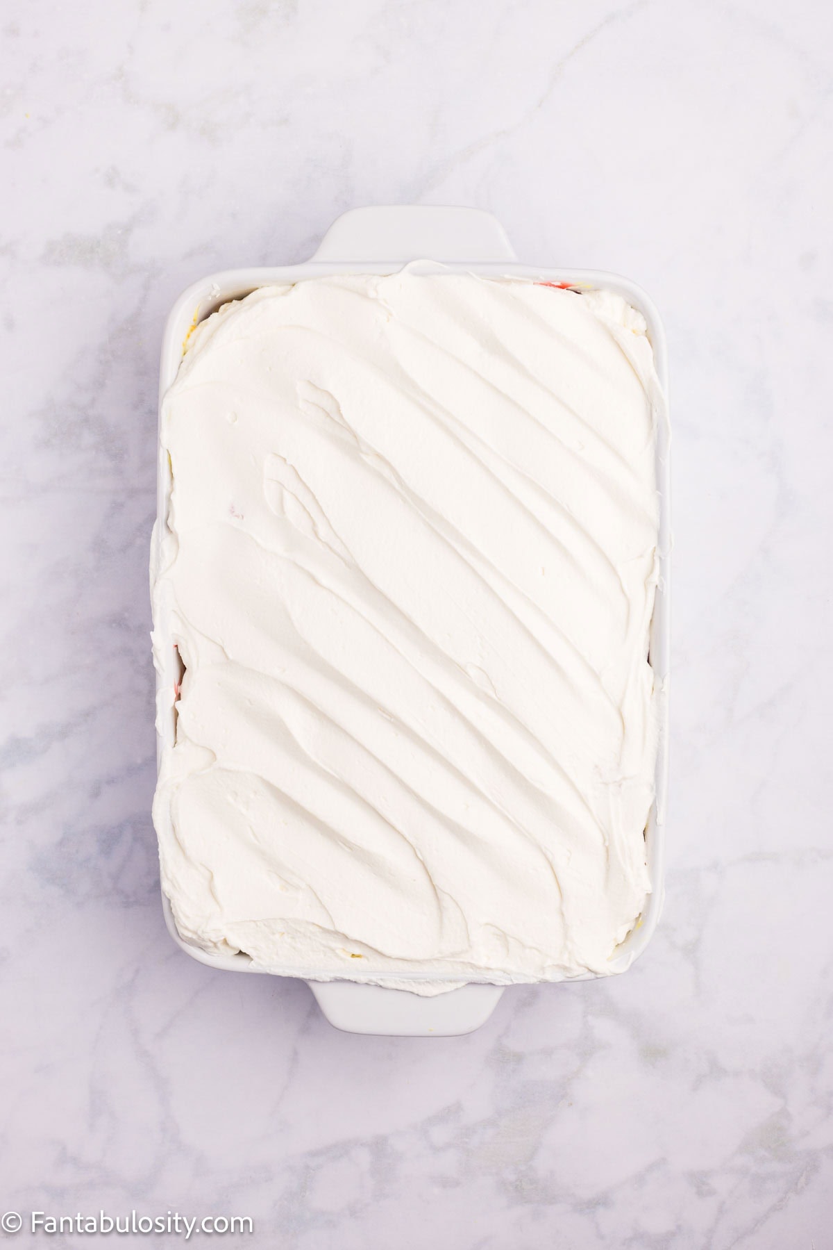 Whipped cream spread on top of strawberry pie filling and angel food cake.