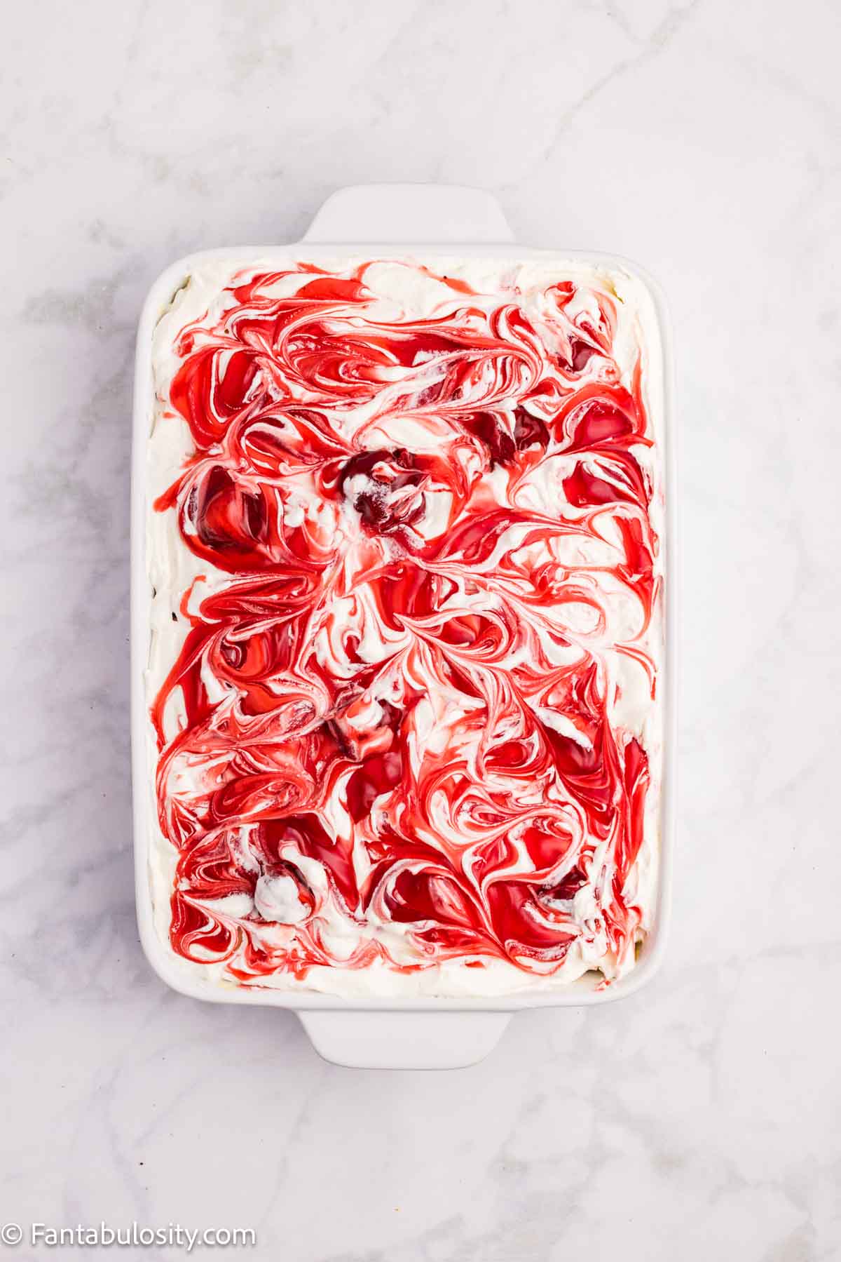 Strawberry pie filling swirled on top of whipped cream in 9x13 baking dish.