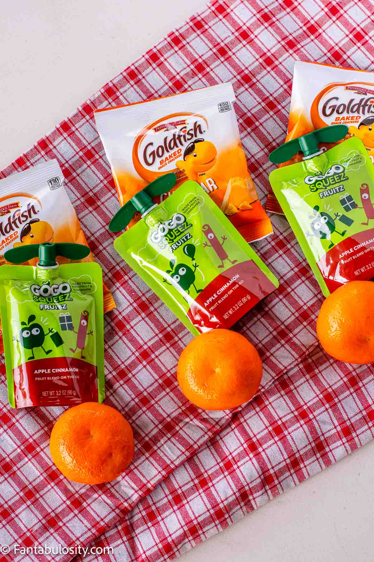 Goldfish cracker packs, applesauce pouches and clementines sitting on table for baseball snacks.