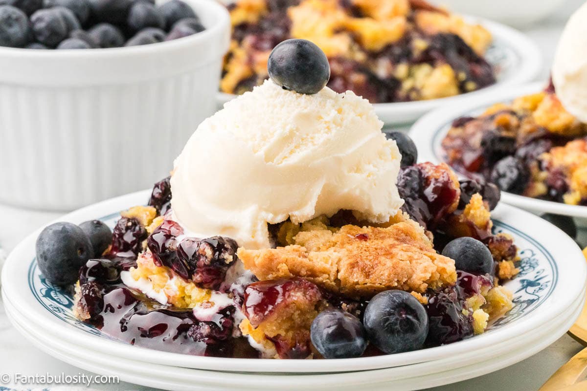 A serving of blueberry dump cake topped with vanilla ice cream, on a plate.