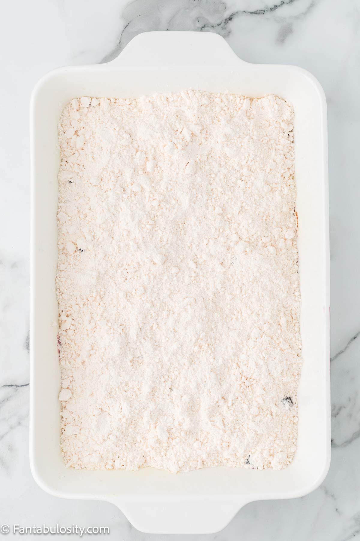 Cake mix sprinkled on top of blueberry pie filling in 9x13 baking dish.