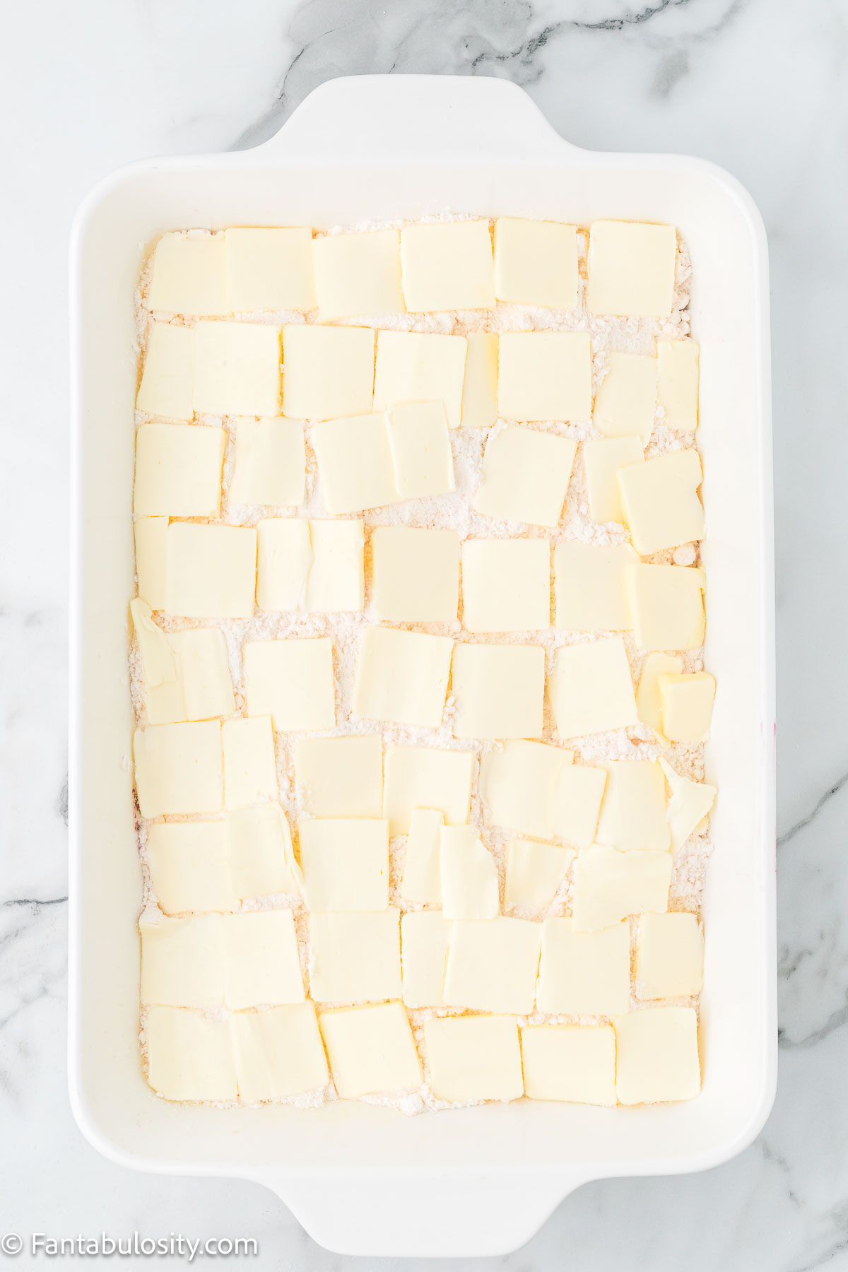 Slices of butter on top of cake mix for blueberry dump cake.