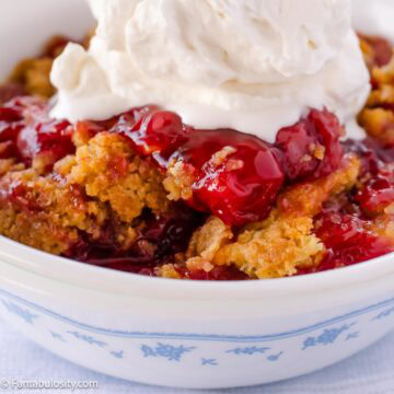 Cherry dump cake topped with homemade whipped cream, served in a dessert bowl.