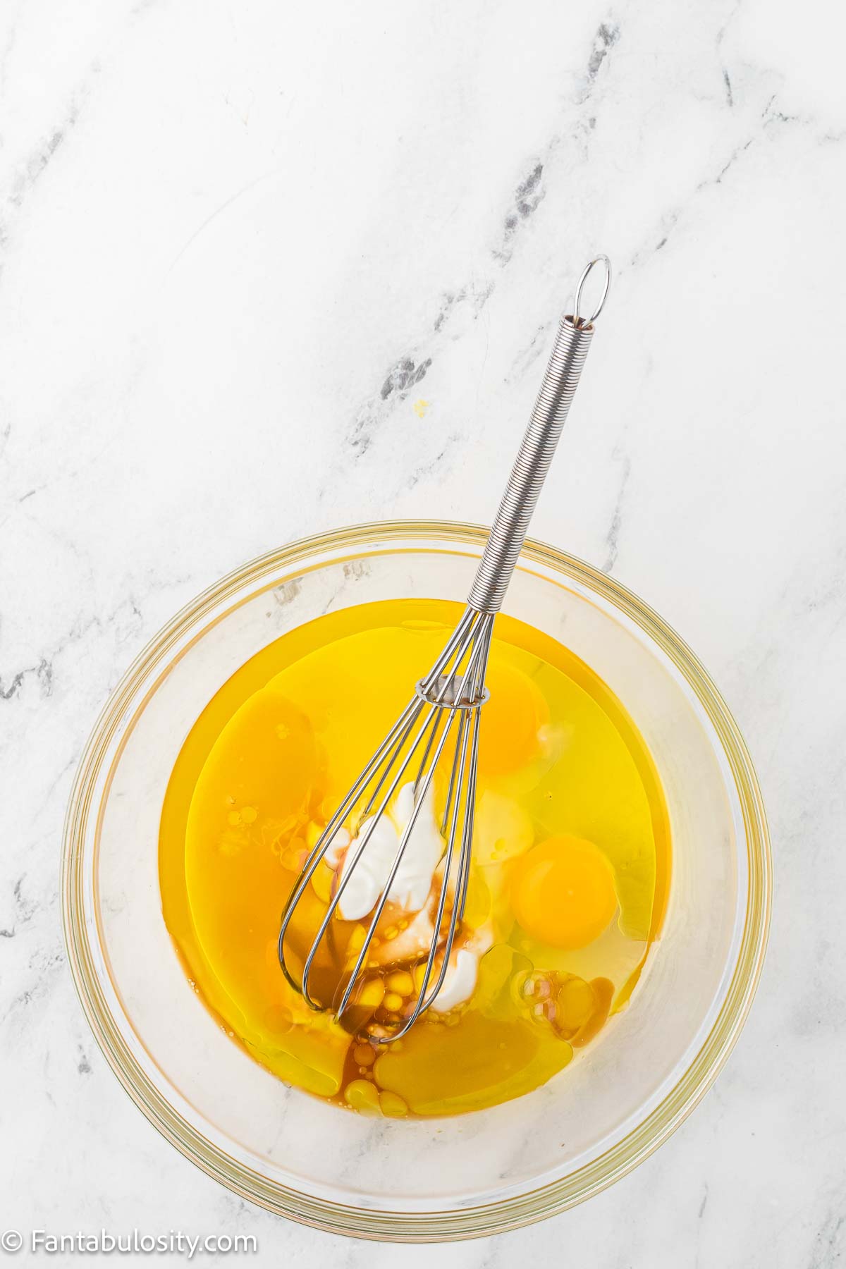 Eggs, yogurt and oil in clear mixing bowl with whisk.