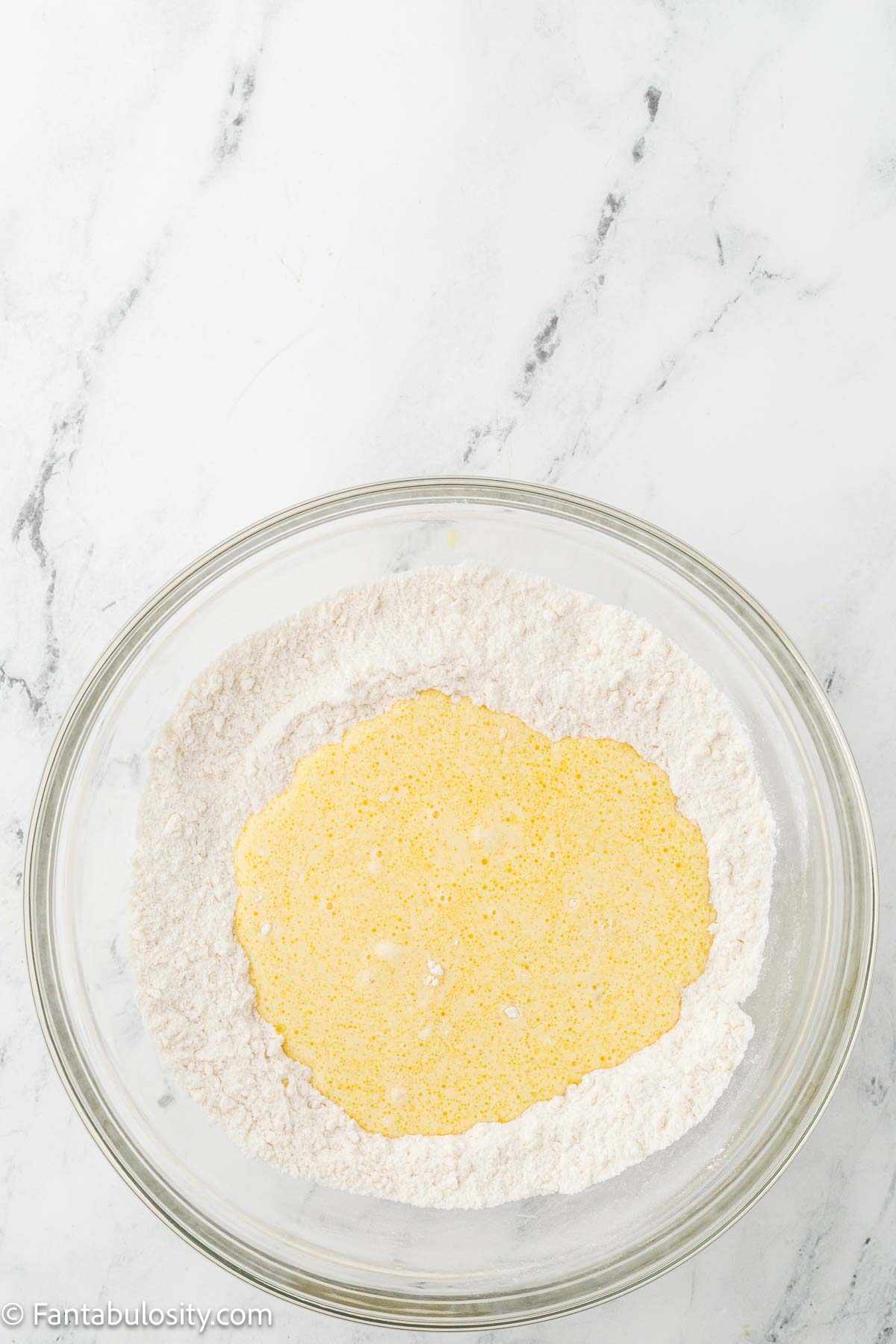 Wet ingredients added to dry ingredients in clear mixing bowl.