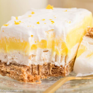 A slice of lemon lush sitting on a clear plate, with a fork bite taken out.
