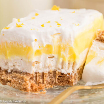 A slice of lemon lush sitting on a clear plate, with a fork bite taken out.