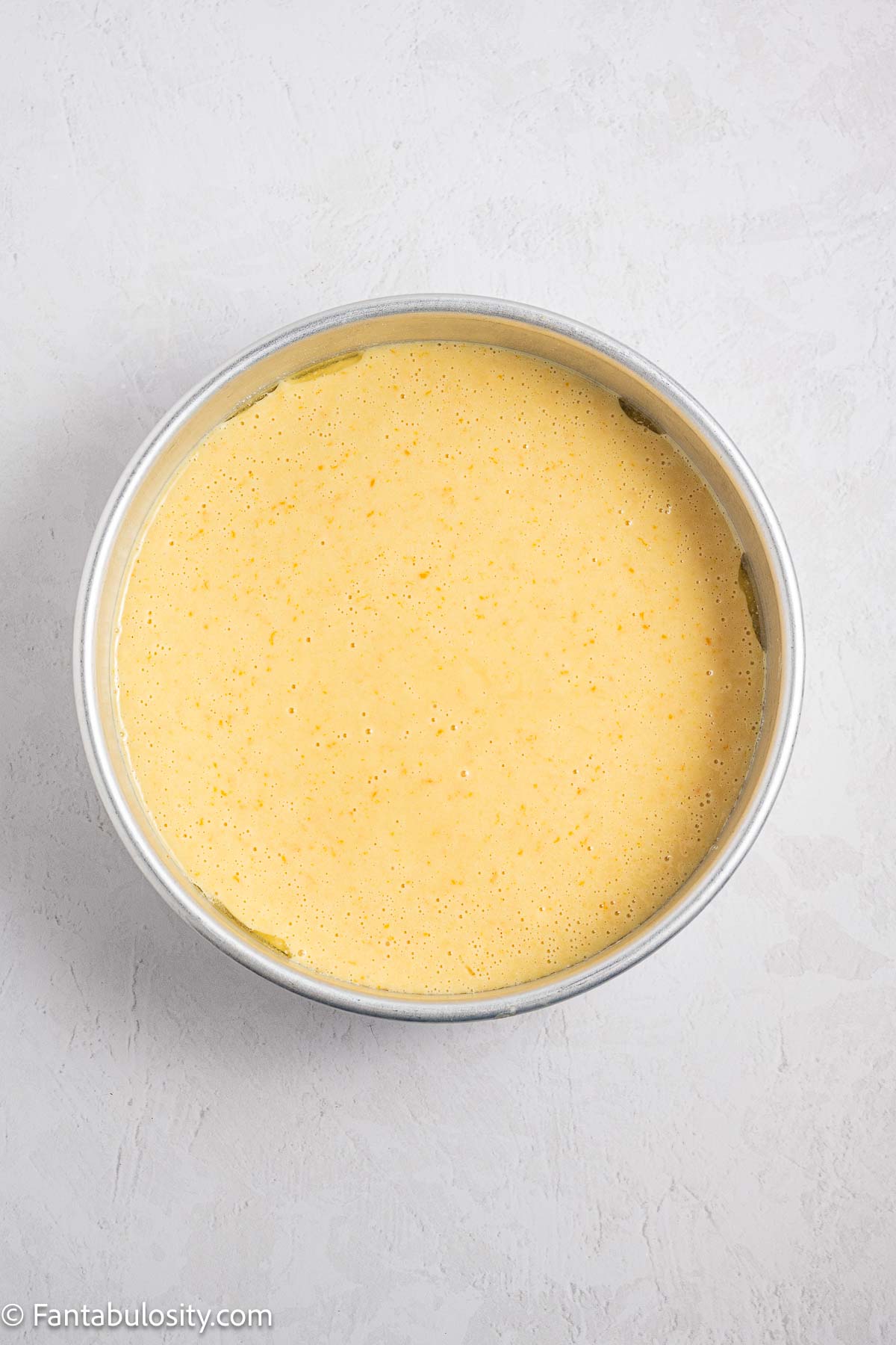 Orange cake batter poured in to round cake pan.