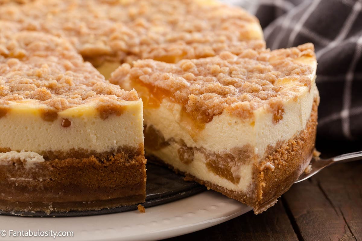 This is a slice of peach cobbler cheesecake being pulled out from rest of cheesecake.