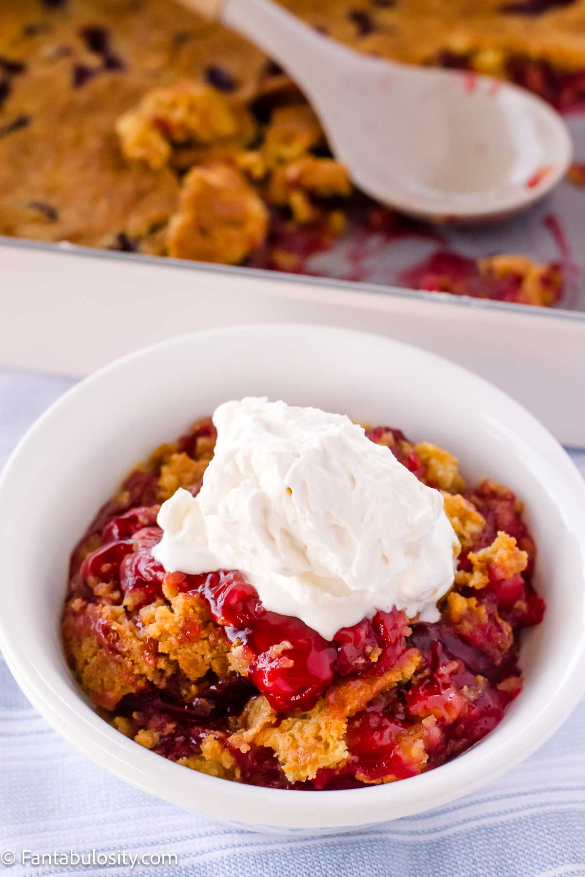 A serving of dump cake in a bowl, topped with a dollop of homemade whipped cream.