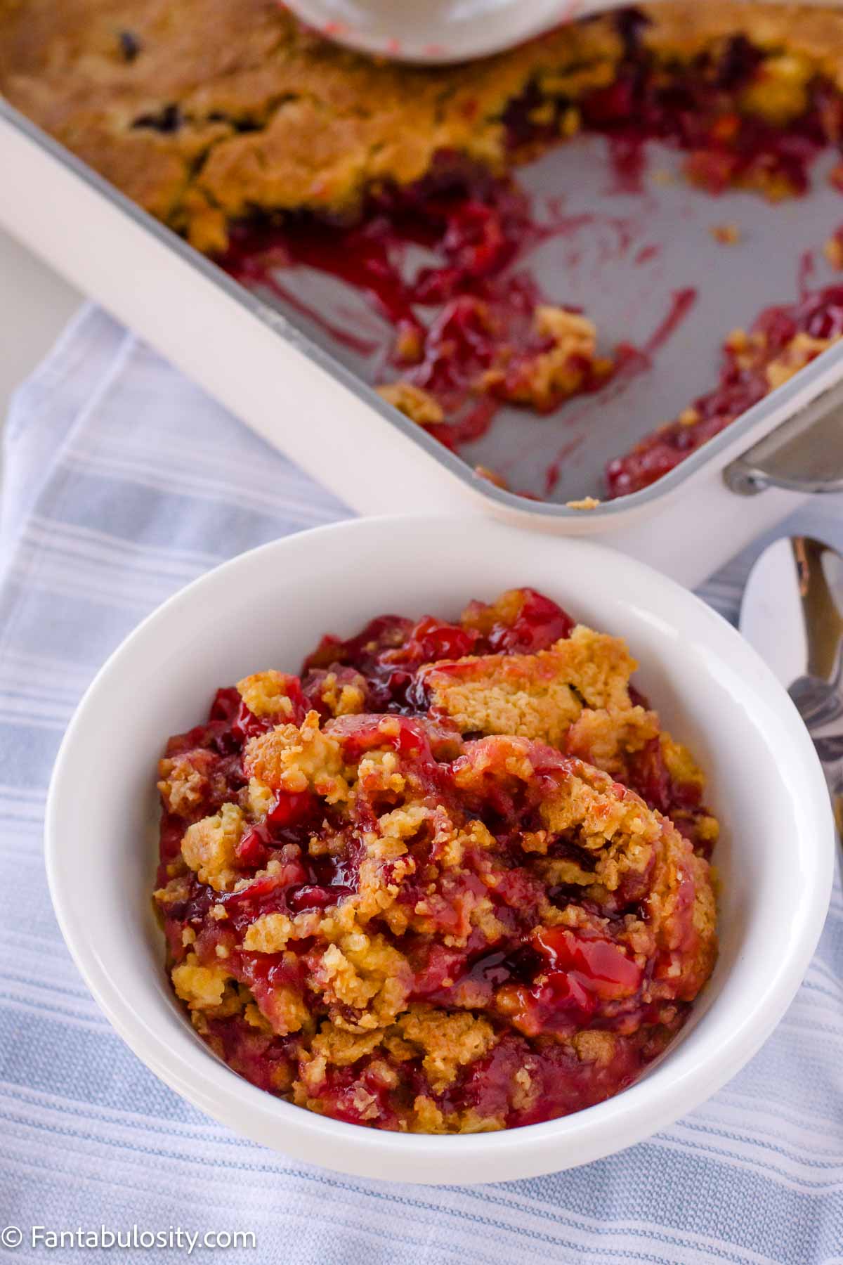 Cherry dump cake served in small serving bowl, sitting next to 9x13 baking dish.