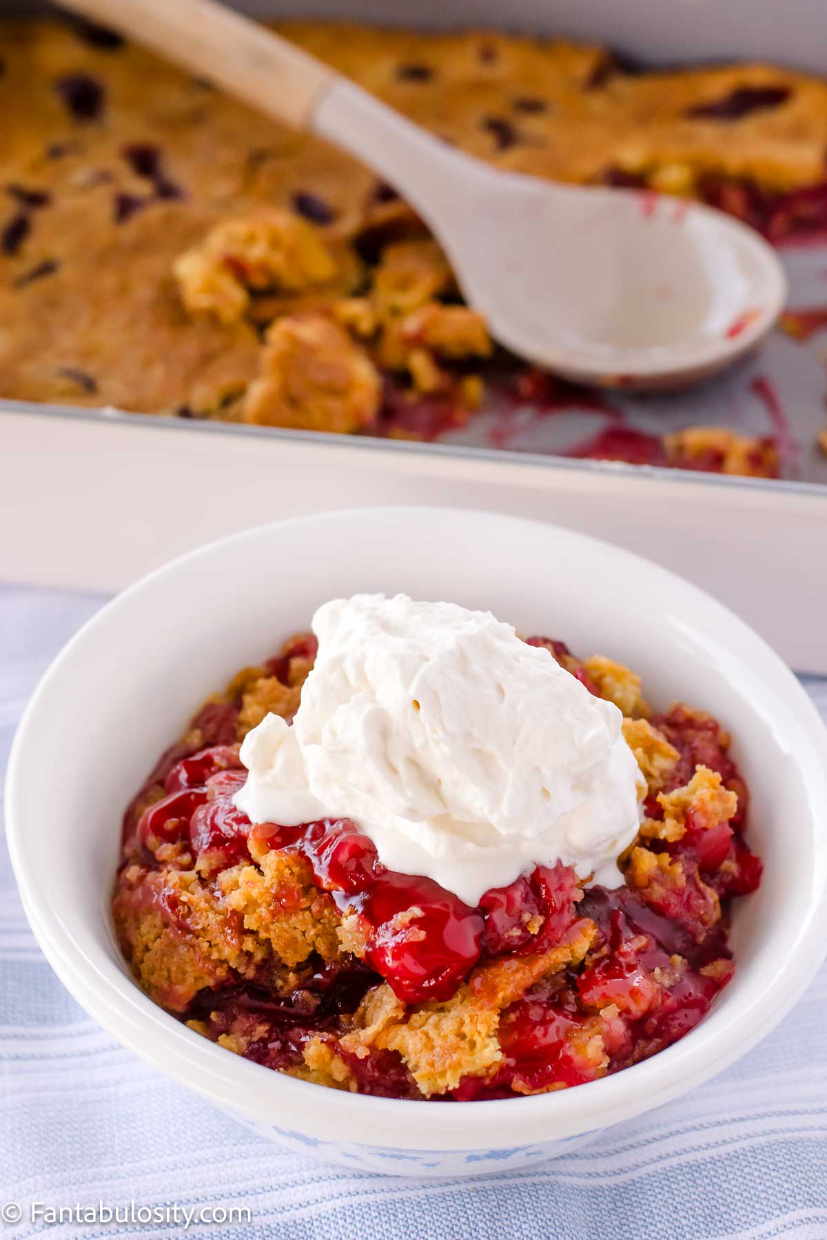 A serving of cherry dump cake in a bowl, with whipped cream spooned on top. 