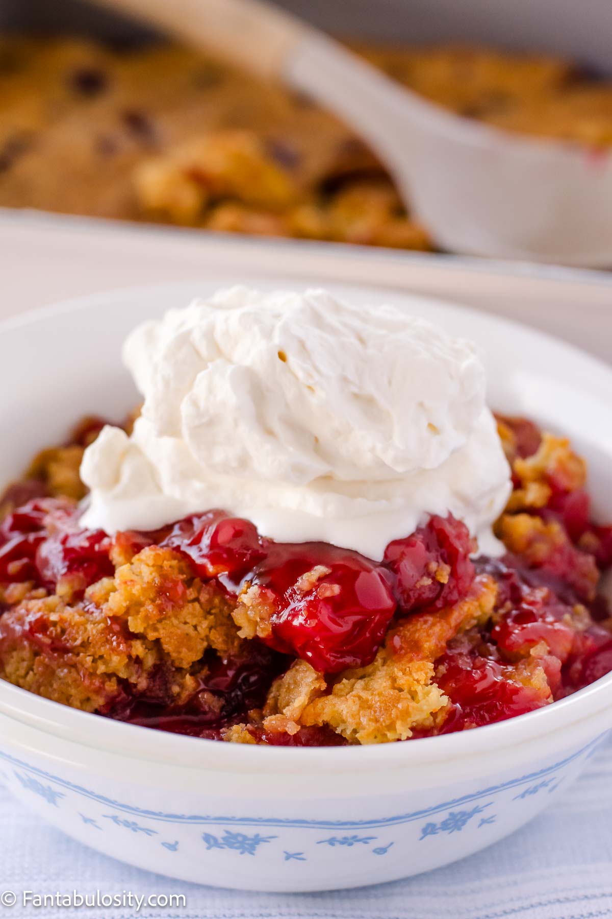 Cherry dump cake, topped with whipped cream, in a vintage bowl.