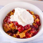 A serving of 3-ingredient dump cake in a bowl with a dollop of homemade whipped cream.