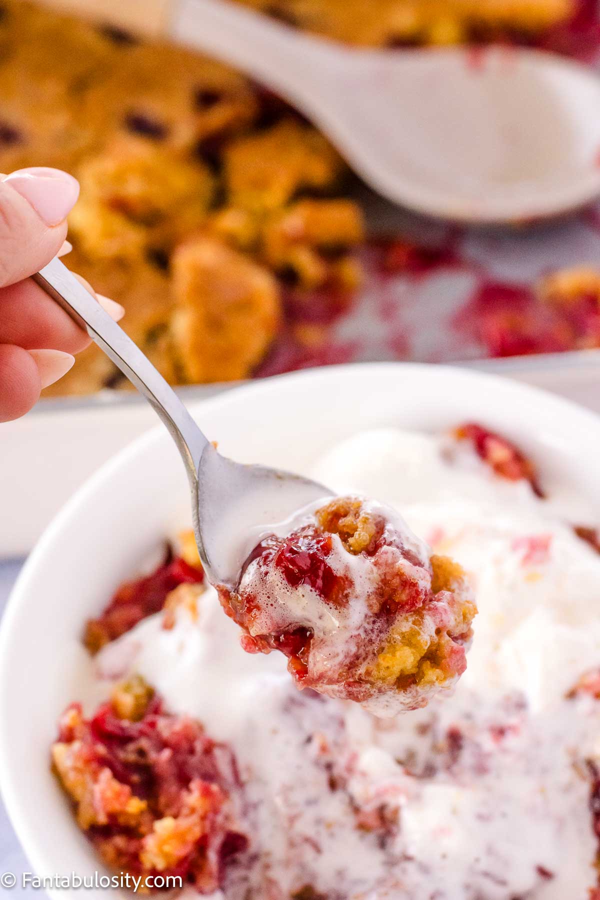 A bite-size of dump cake being held by spoon, above bowl.