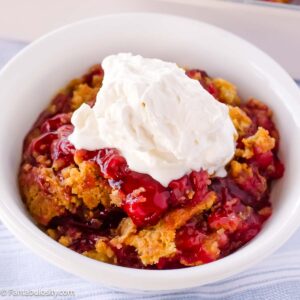 A serving of 3-ingredient dump cake in a bowl with a dollop of homemade whipped cream.