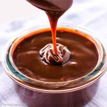 Hot fudge sauce dripping from spoon in to bowl.