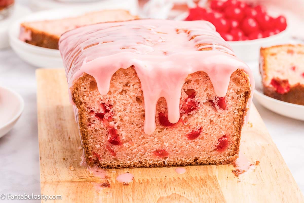 Cherry bread with cherry icing on wooden cutting board.