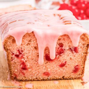 Cherry bread with cherry icing on wooden cutting board.