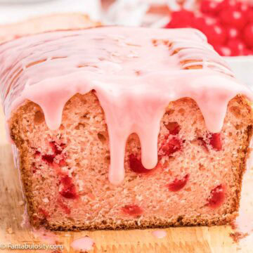 Cherry bread with cherry icing on wooden cutting board.