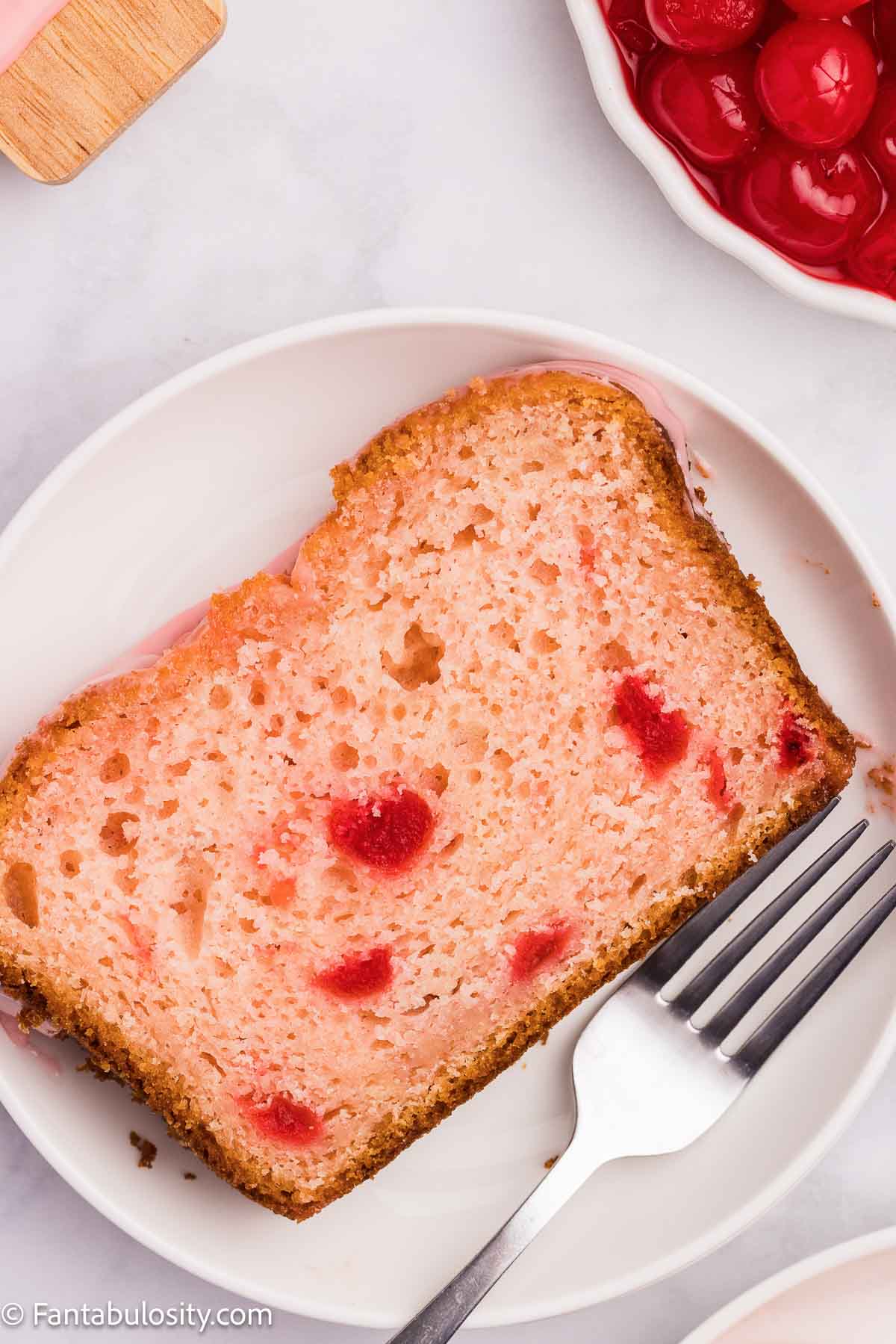 A slice of cherry bread resting on a plate, next to a fork.