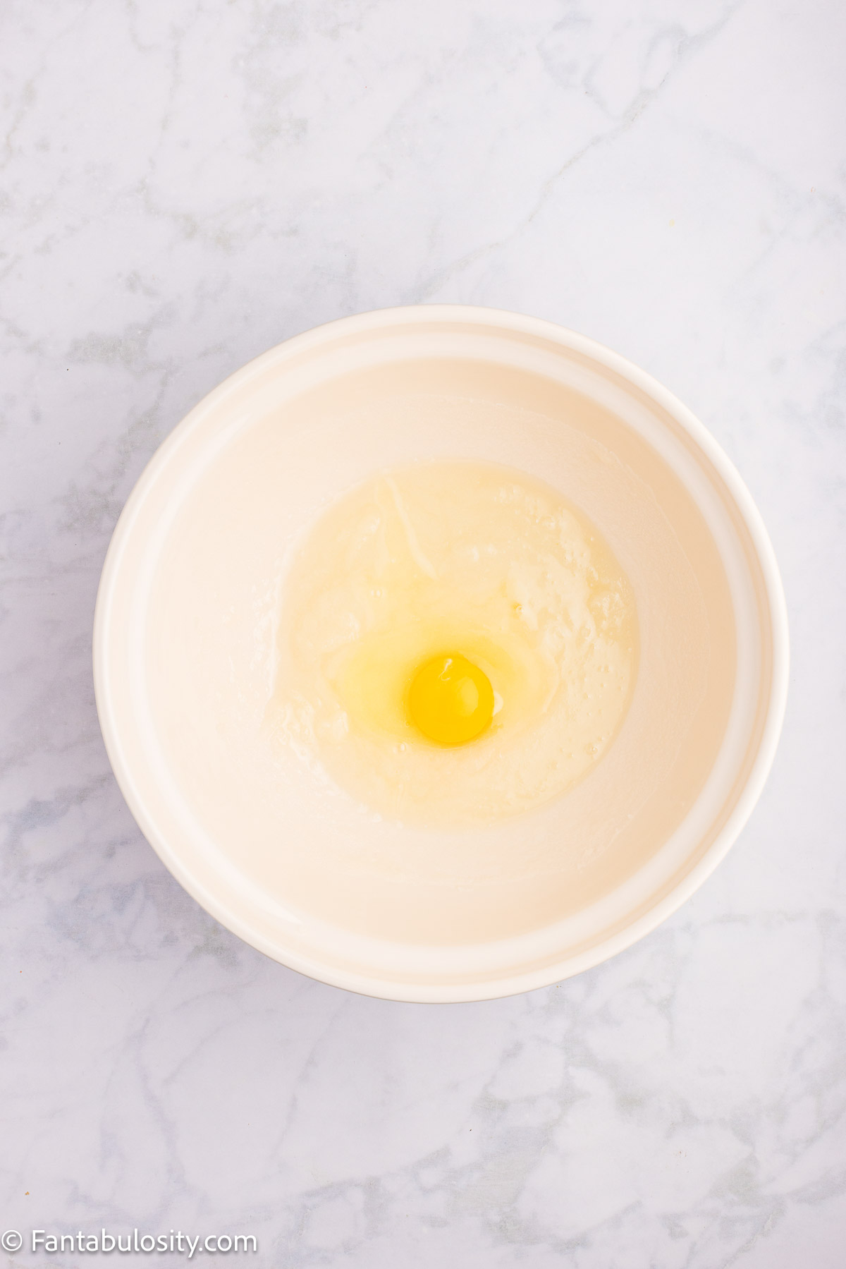 Egg added in to sugar and oil in mixing bowl for cherry bread recipe.