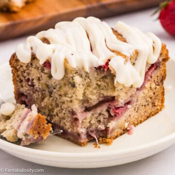 A slice of strawberry banana cake with cream cheese frosting drizzled on top.
