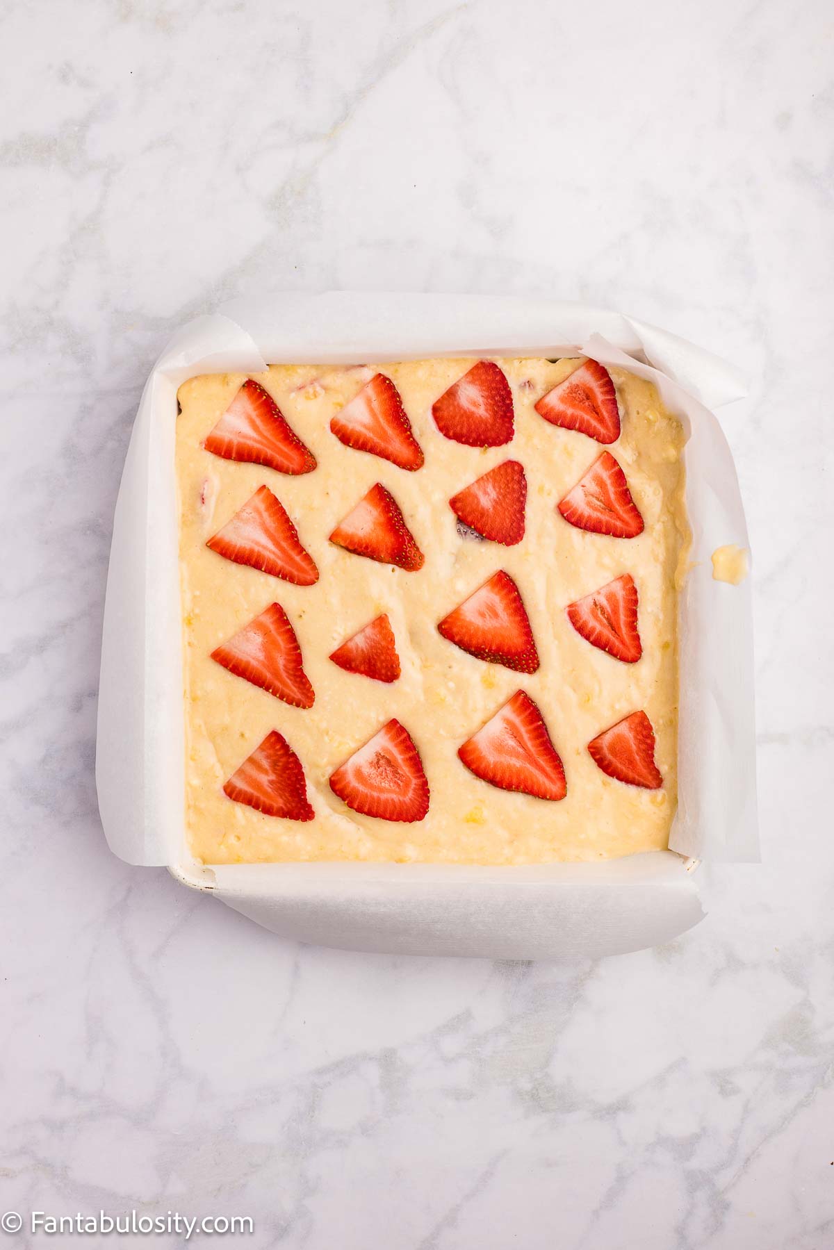 Strawberry banana cake batter in 8x8 baking dish, with strawberries on top.