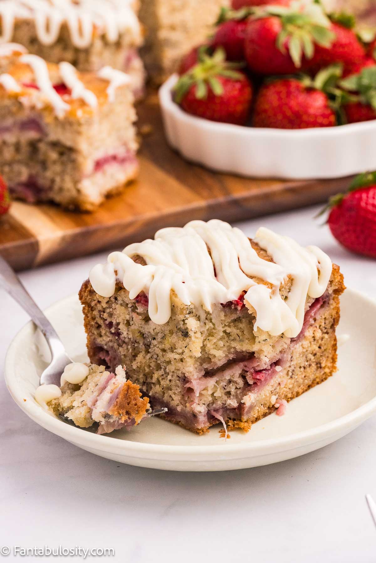 A slice of strawberry banana cake on round plate with fork.
