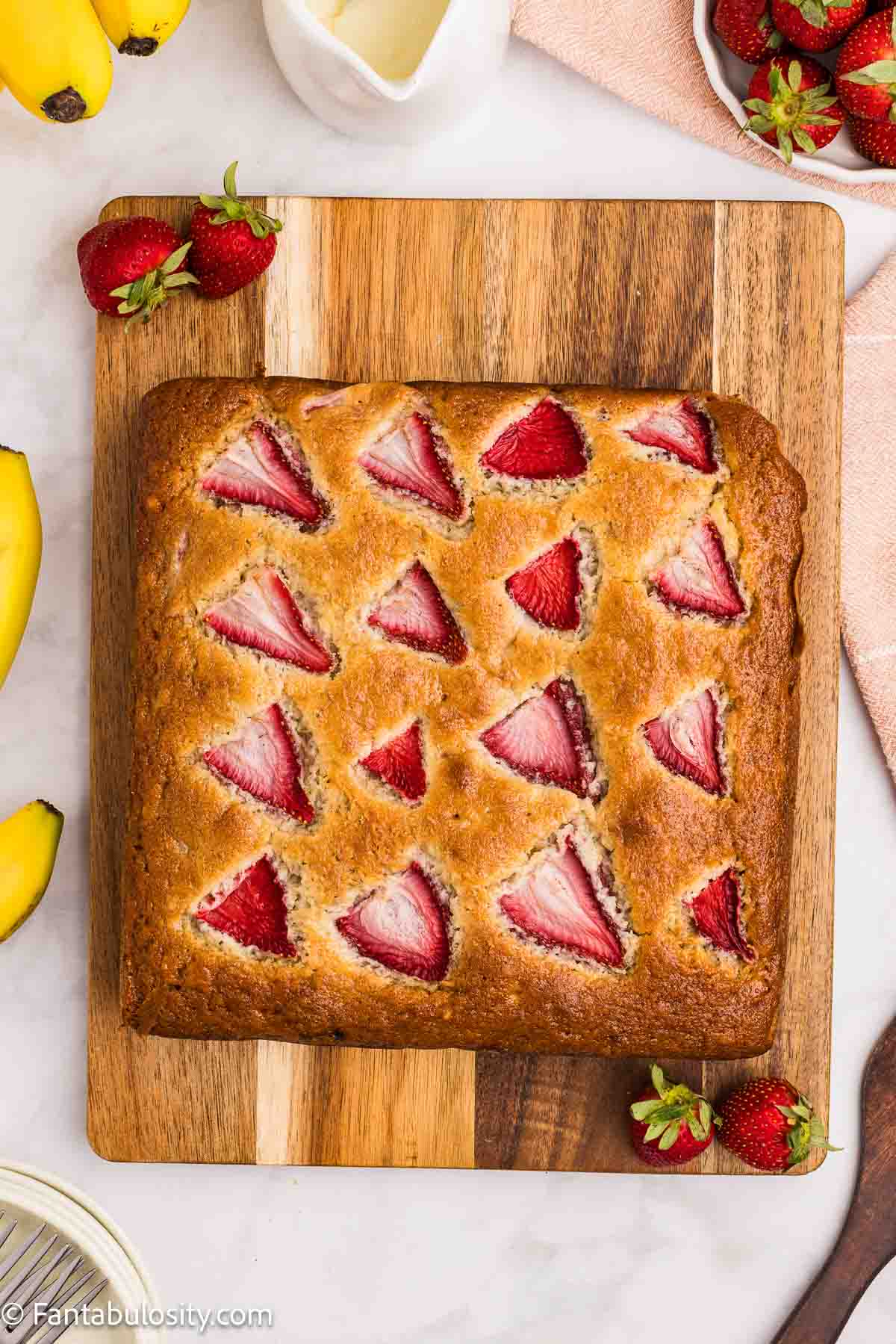 Baked banana strawberry cake on wooden cutting board.