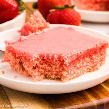 Slice of strawberry Texas sheet cake on a round plate, with a bite taken out.