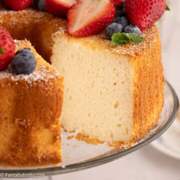 Angel food cake on cake stand, that's topped with fruit.