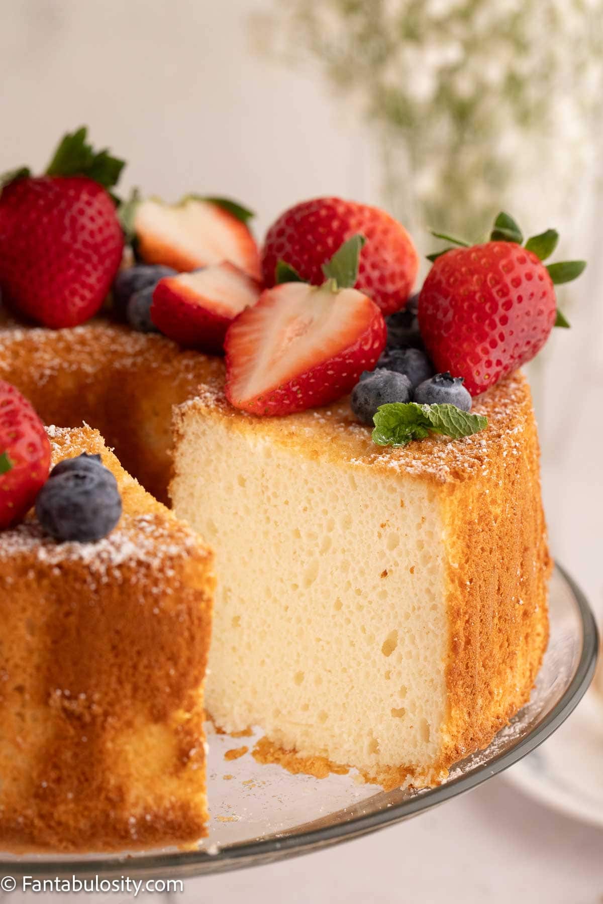 Angel food cake on cake stand, topped with fruit.