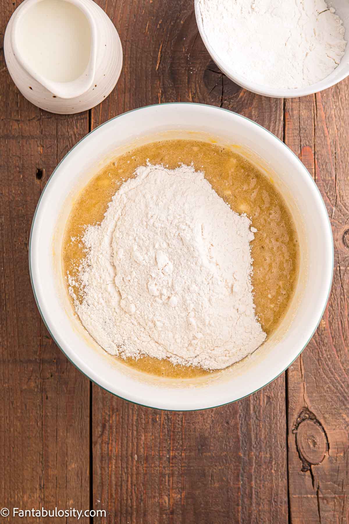 Flour mixture added to wet ingredients in mixing bowl for banana cake.