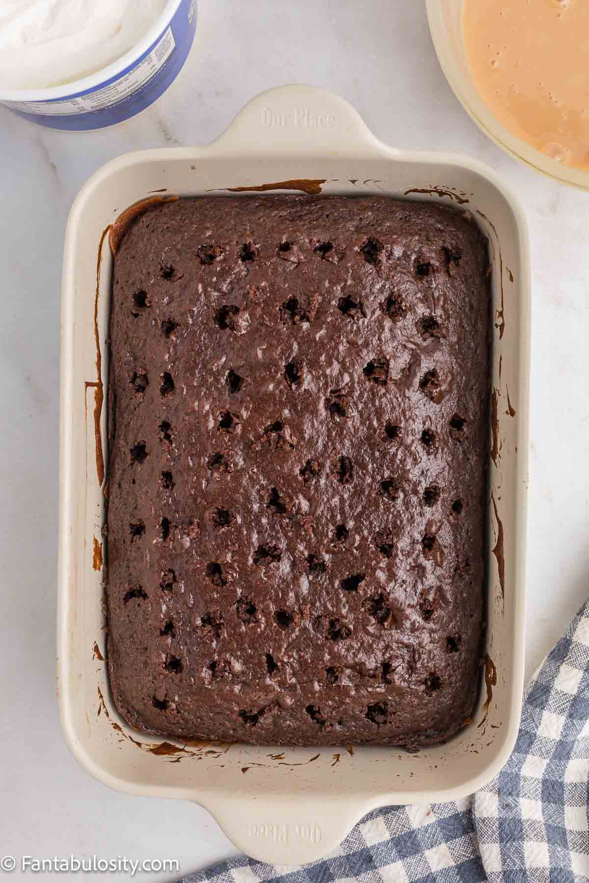 Chocolate cake in 9x13 baking dish that was poked with wooden spoon.