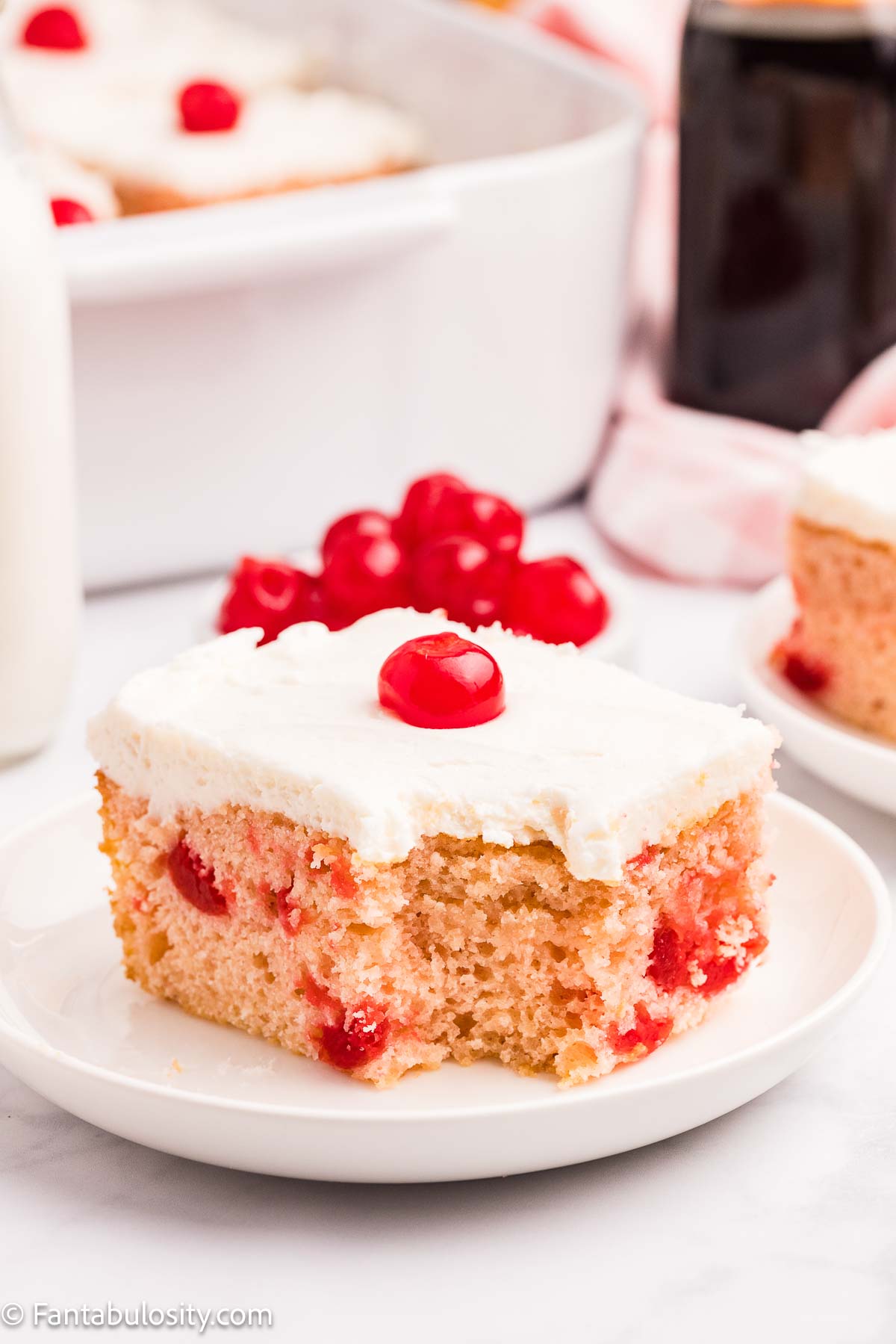 A slice of cherry cake on a plate, with a bite taken out.